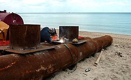 Worker welding 30-inch pipe to to carry sand onto beach from Pumpout Station